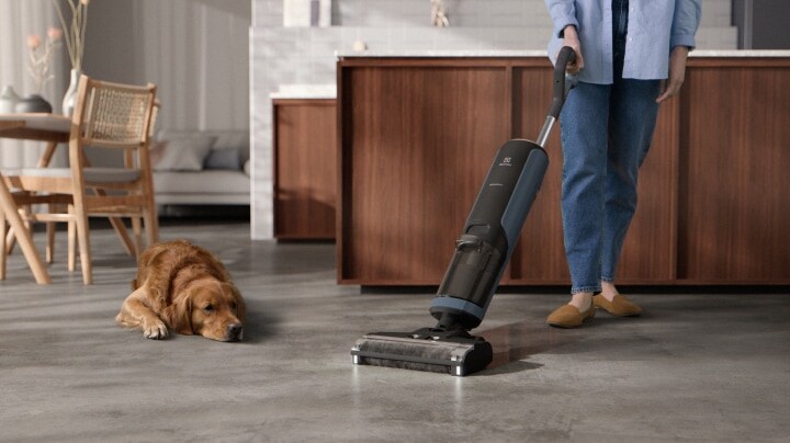 A person cleaning the house with a vacuum cleaner and a dog laying beside